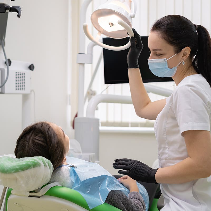 Caucasian woman dentist doctor in office with dental equipment microscope treats teeth to patient in chair